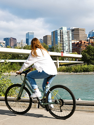a woman rides a bike along the bow river in downtown Calgary